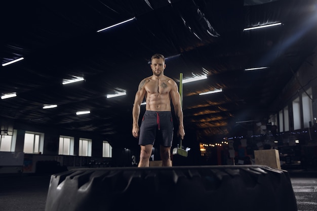 Jeune homme en bonne santé, athlète faisant des exercices d'équilibre dans la salle de gym. Modèle unique s'entraînant dur, s'entraînant avec le pneu. Concept de mode de vie sain, sport, fitness, musculation, bien-être.