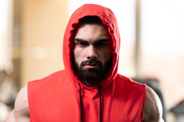 Jeune homme en bonne santé debout fort dans la salle de gym et muscles de la flexion dans un sweat à capuche rouge Muscular Athletic Bodybuilder Fitness Model Posing After Exercises