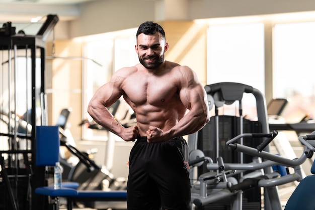 Jeune homme en bonne santé debout fort dans la salle de gym et muscles de la flexion Muscular Athletic Bodybuilder Fitness Model Posing After Exercises