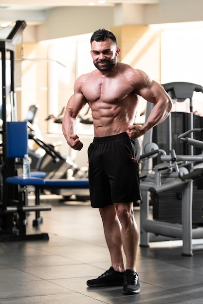 Jeune homme en bonne santé debout fort dans la salle de gym et muscles de la flexion Muscular Athletic Bodybuilder Fitness Model Posing After Exercises