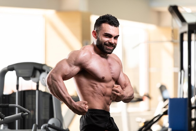 Jeune homme en bonne santé debout fort dans la salle de gym et muscles de la flexion Muscular Athletic Bodybuilder Fitness Model Posing After Exercises