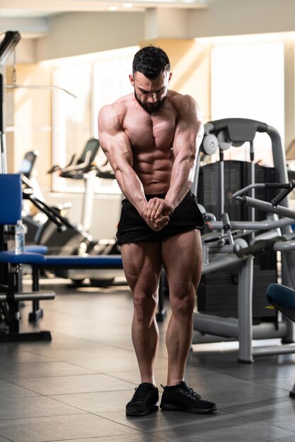 Jeune homme en bonne santé debout fort dans la salle de gym et muscles de la flexion Muscular Athletic Bodybuilder Fitness Model Posing After Exercises