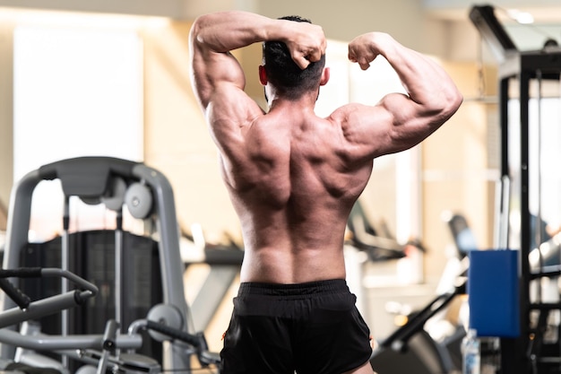 Jeune homme en bonne santé debout fort dans la salle de gym et muscles de la flexion Muscular Athletic Bodybuilder Fitness Model Posing After Exercises