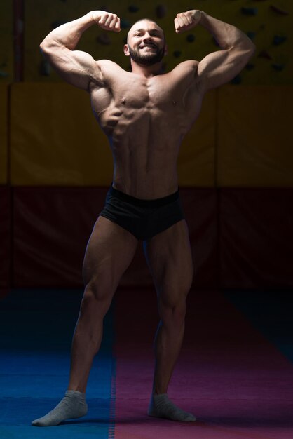 Jeune homme en bonne santé debout fort dans la salle de gym et muscles de la flexion Muscular Athletic Bodybuilder Fitness Model Posing After Exercises