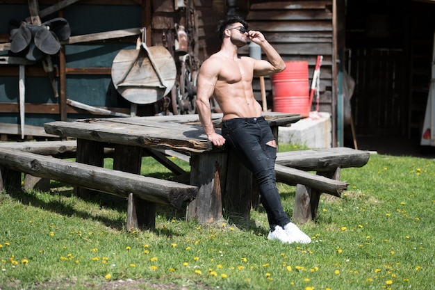 Jeune homme en bonne santé debout avec des muscles fléchissants forts tout en portant un jean noir Modèle de forme physique de bodybuilder athlétique musclé posant à l'extérieur une place pour votre texte