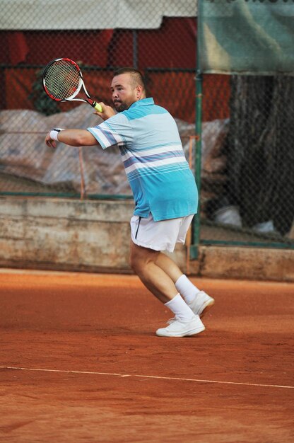 Un jeune homme en bonne santé joue au tennis avec un ami à l'extérieur.