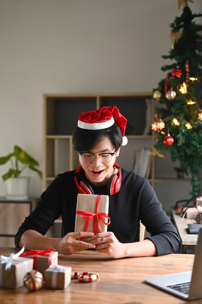 Jeune homme en bonnet de Noel préparant des cadeaux de Noël dans le salon.