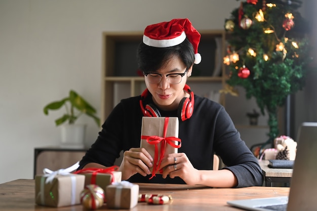 Jeune homme en bonnet de Noel tenant des cadeaux de Noël avec ruban rouge.