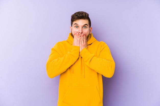 Jeune homme sur la bouche couvrant violet choqué avec les mains.