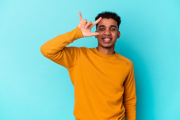 Jeune homme bouclé afro-américain isolé sur bleu montrant un geste de cornes comme un concept de révolution.