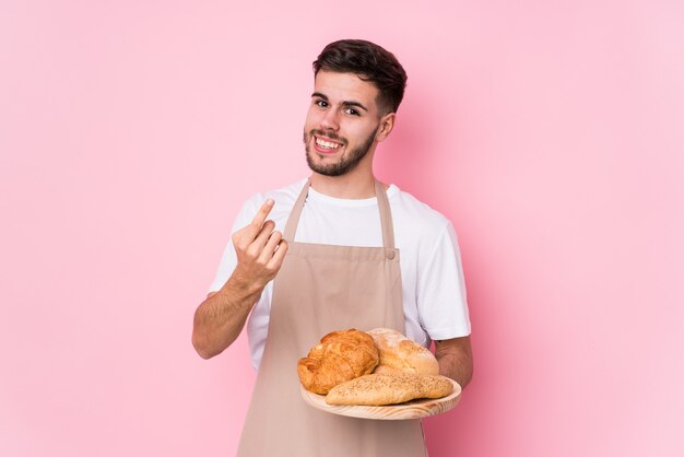Jeune homme de boulanger caucasien pointant avec le doigt vers vous comme si invitant à se rapprocher.