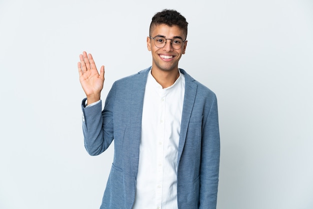 Jeune homme brésilien d'affaires isolé sur mur blanc saluant avec la main avec une expression heureuse