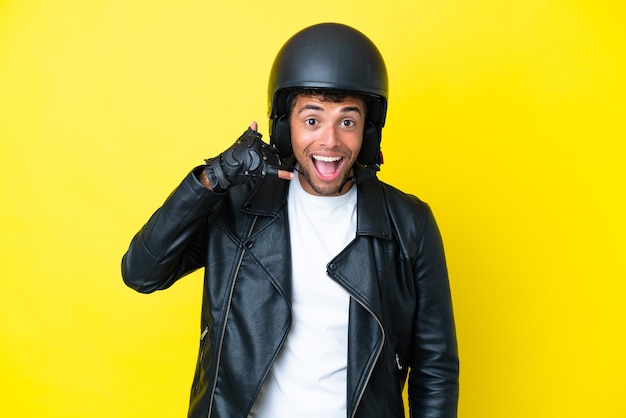 Jeune homme brésilien avec un casque de moto isolé sur fond jaune faisant un geste de téléphone Call me back sign