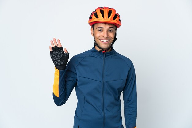 Jeune homme brésilien cycliste isolé sur fond blanc saluant avec la main avec une expression heureuse