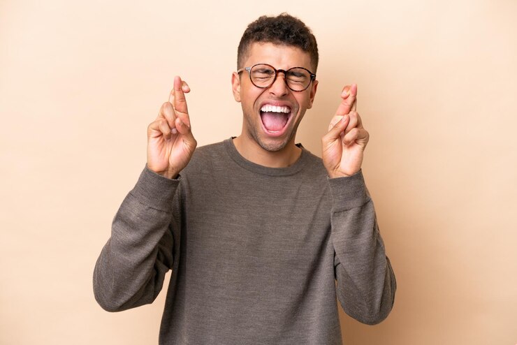 Photo jeune homme brésilien isolé sur fond beige avec les doigts croisés