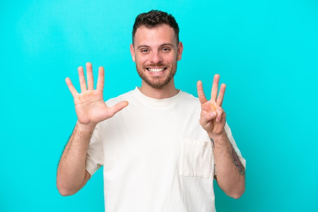 Jeune homme brésilien isolé sur fond bleu comptant huit avec les doigts