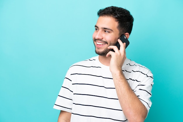 Jeune homme brésilien isolé sur fond bleu en gardant une conversation avec le téléphone mobile avec quelqu'un