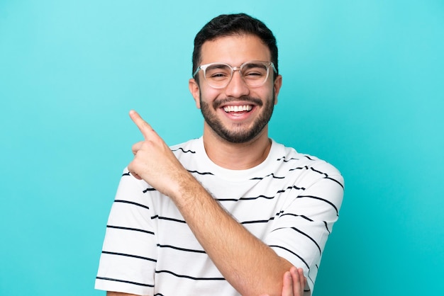 Jeune homme brésilien isolé sur fond bleu avec des lunettes et côté pointant