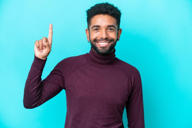 Jeune homme brésilien isolé sur fond bleu pointant vers le haut une excellente idée