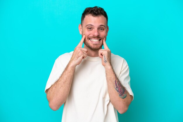Jeune homme brésilien isolé sur fond bleu souriant avec une expression heureuse et agréable