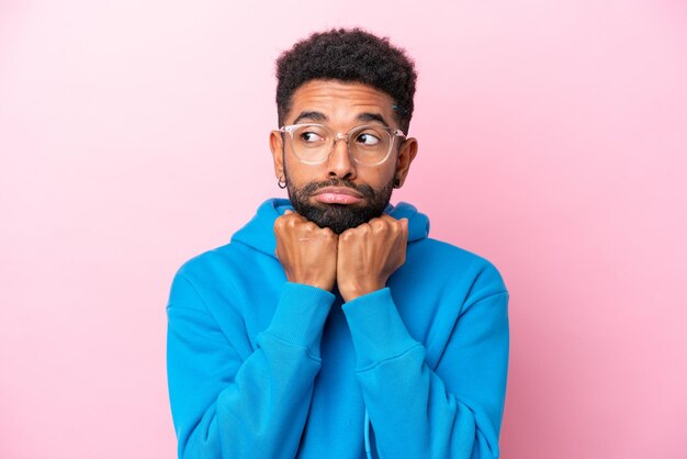 Jeune homme brésilien isolé sur fond rose avec des lunettes et fatigué