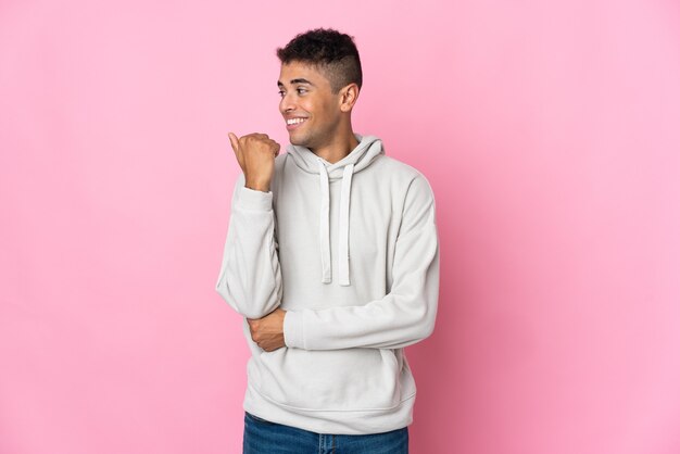 Jeune homme brésilien isolé sur un mur rose pointant vers le côté pour présenter un produit