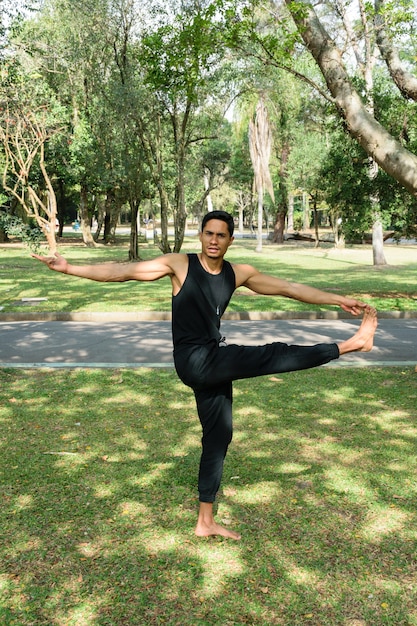 Jeune homme brésilien pratiquant le yoga dans une position équilibrée dans un parc public par une journée ensoleillée.