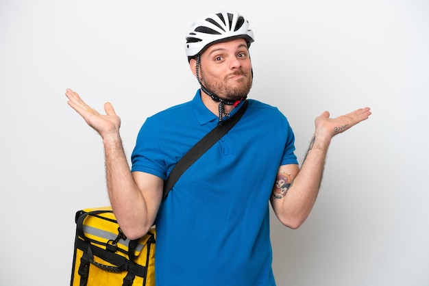 Jeune homme brésilien avec sac à dos thermique isolé sur fond blanc ayant des doutes tout en levant les mains