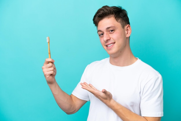 Jeune homme brésilien se brosser les dents isolé sur fond bleu étendant les mains sur le côté pour inviter à venir