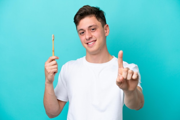 Jeune homme brésilien se brosser les dents isolé sur fond bleu montrant et levant un doigt