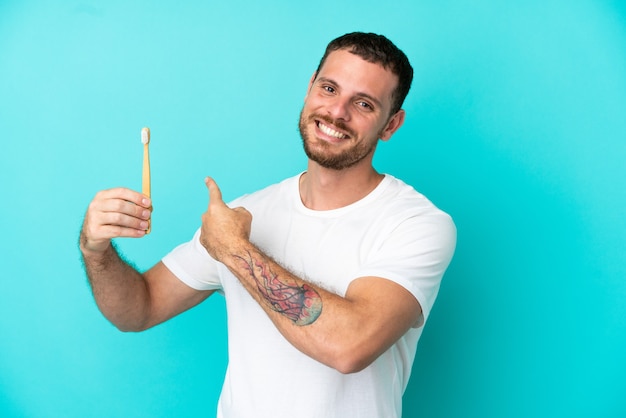 Jeune homme brésilien se brosser les dents isolé sur fond bleu pointant vers l'arrière