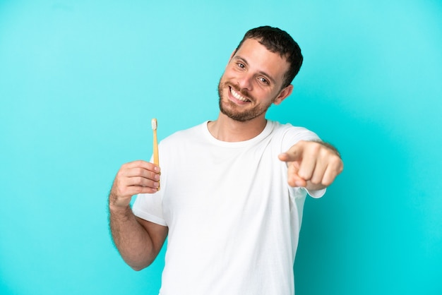 Jeune homme brésilien se brosser les dents isolé sur fond bleu pointant vers l'avant avec une expression heureuse