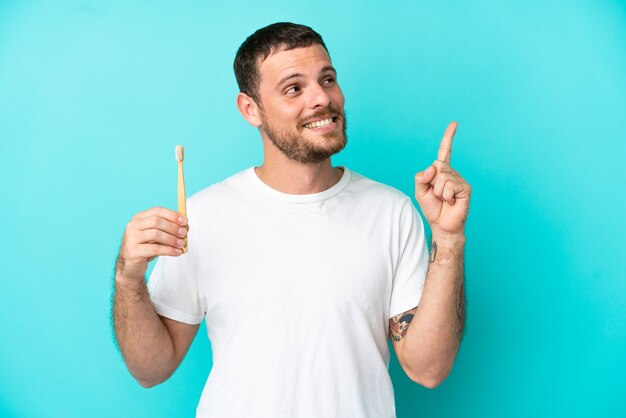 Jeune homme brésilien se brosser les dents isolé sur fond bleu pointant vers une excellente idée