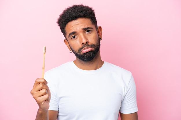 Jeune homme brésilien se brosser les dents isolé sur fond rose avec une expression triste