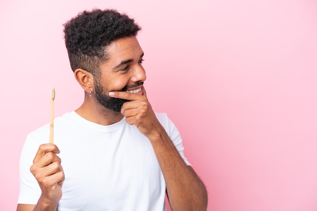 Jeune homme brésilien se brosser les dents isolé sur fond rose en pensant à une idée et en regardant de côté