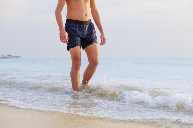 Jeune homme bronzé en short de bain mouillé se promène au bord de la mer