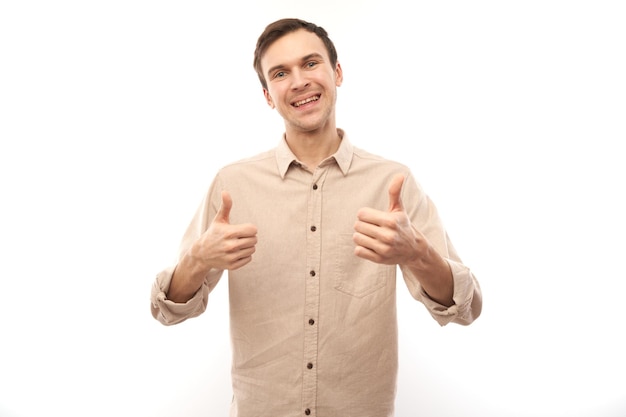 Jeune homme brune montre la main avec les pouces vers le haut et sourit à la caméra isolée sur fond blanc