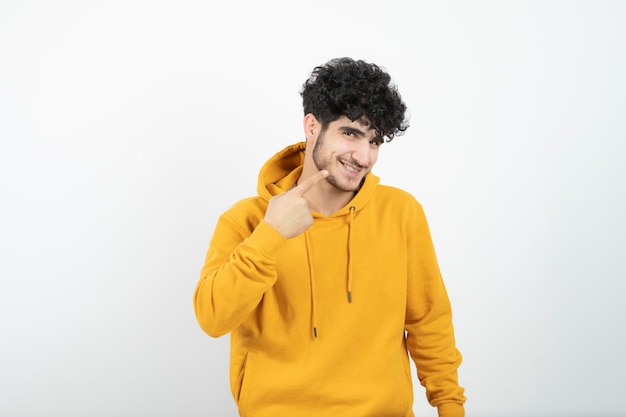 jeune homme brune en sweat à capuche jaune debout et pointant vers son sourire.