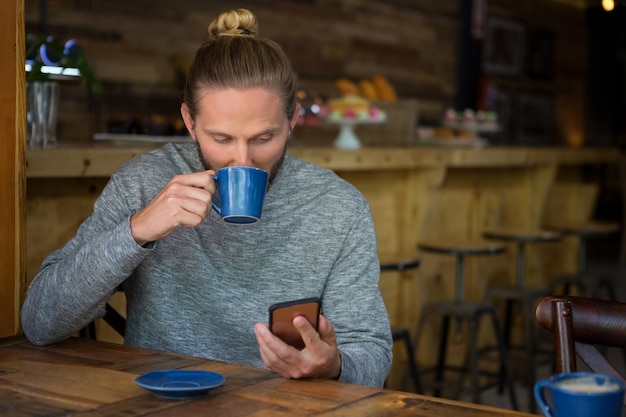 Jeune homme buvant du café tout en utilisant un téléphone intelligent au café