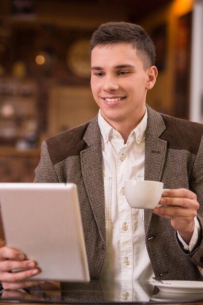 Jeune homme buvant du café et en utilisant une tablette au café.