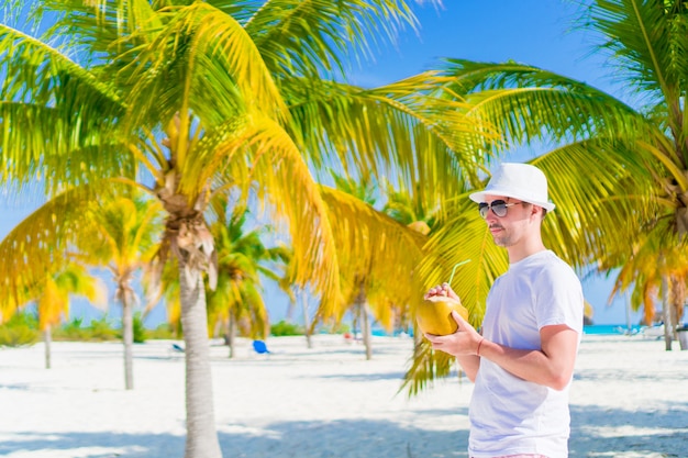 Jeune homme buvant du lait de coco par une journée chaude sur la plage de la palmeraie