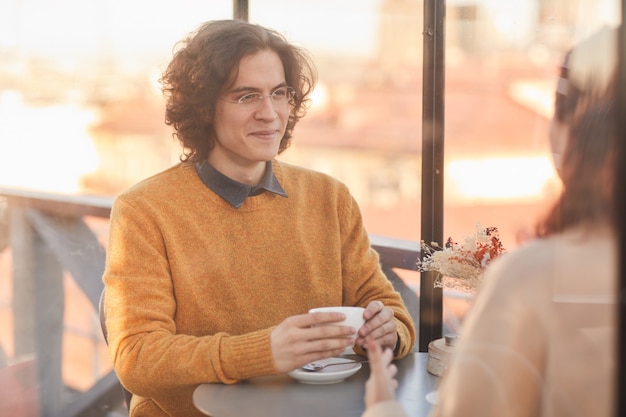 Jeune homme buvant du thé pendant la conversation avec son ami lors d'une réunion au café