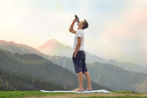 Jeune homme buvant de l'eau au sommet de la montagne après la pratique du yoga