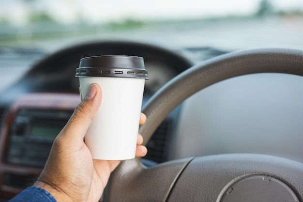 Jeune homme buvant une tasse de café chaud en conduisant une voiture pour voyager Mains tenant le volant