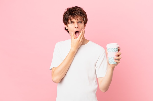 Jeune homme avec un café avec la bouche et les yeux grands ouverts et la main sur le menton