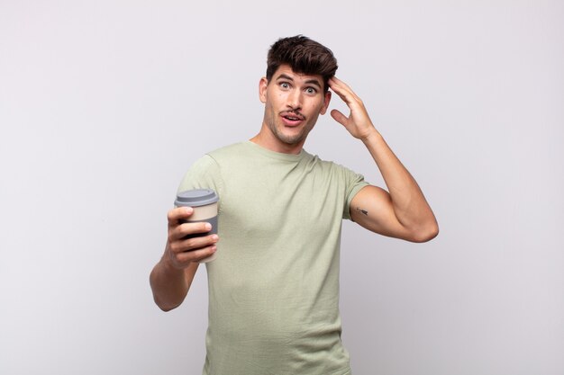 Jeune homme avec un café à la recherche de plaisir, étonné et surpris, souriant et réalisant une bonne nouvelle incroyable et incroyable