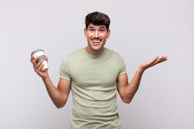 Jeune homme avec un café se sentant heureux, excité, surpris ou choqué, souriant et étonné de quelque chose d'incroyable