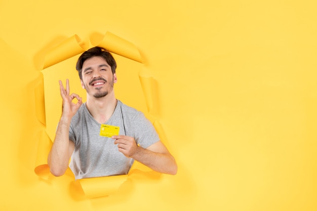 jeune homme avec carte de crédit sur fond de papier jaune déchiré argent vente shopping