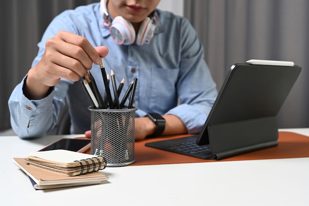 Jeune homme avec casque assis au bureau à domicile et travaillant avec une tablette informatique.