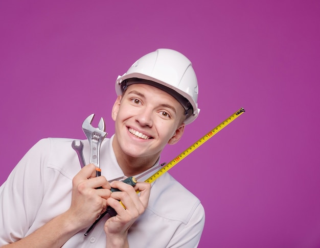 Jeune homme en casque blanc avec outil de travail à la main sur fond violet